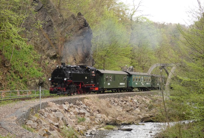 99 1734 vor dem P 5002 nun wieder ganz hoch fahrend mit Kipsdorf als Ziel, fotografiert an der bestens bekannten Weißeritz-Brücke hinter Rabenau, um 13:48h am 22.04.2025
