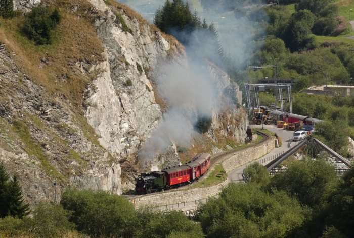Lok 704 mit Zug Nr.133 nach Oberwald in den Kurven an den Felsen im Furka-Reuss-Tal hinter dem Betriebswerk Realp, um 10:22h am 14.08.2022